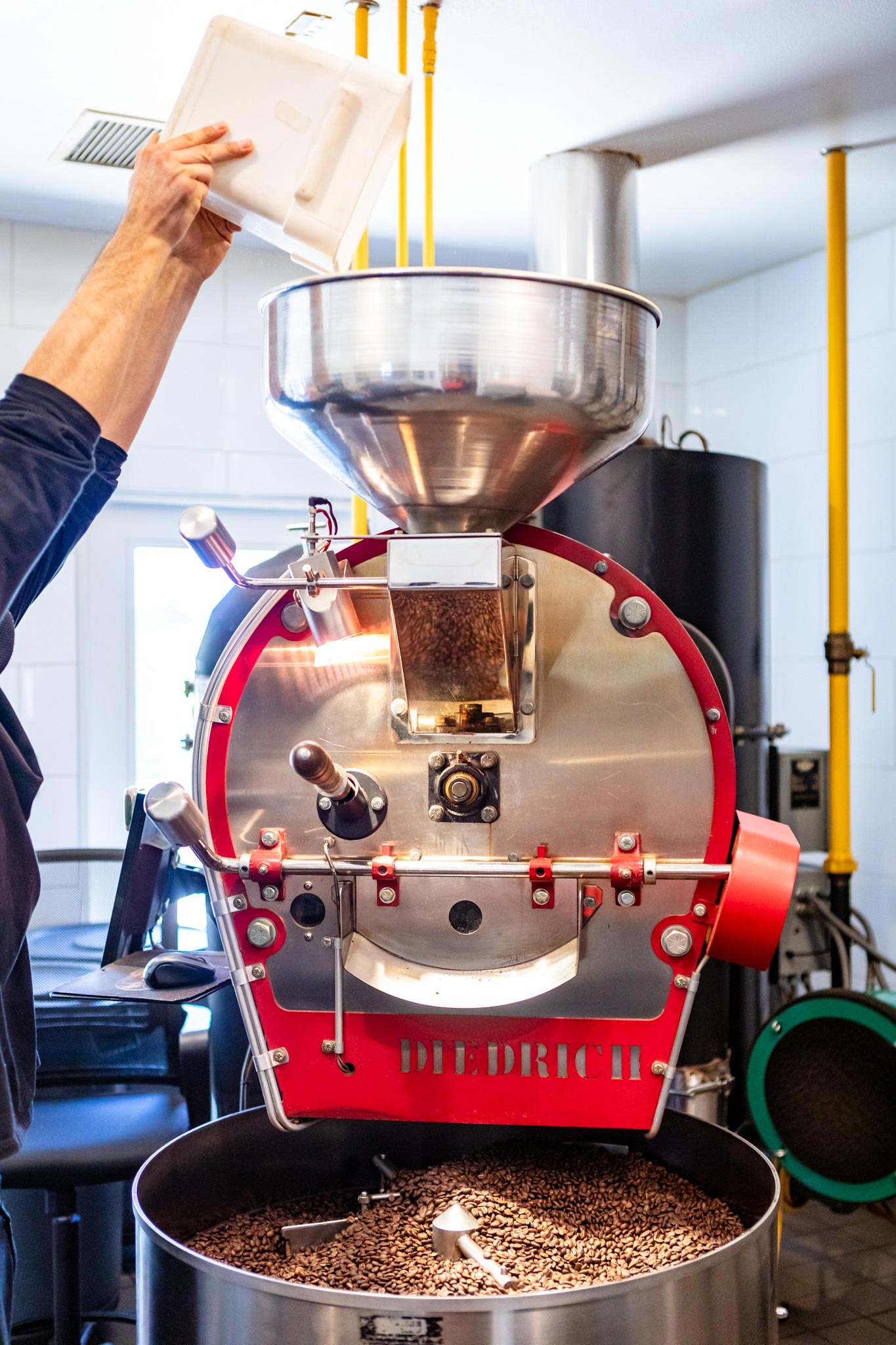 A red coffee roasting machine with beans being dumped into the hopper by a Koffi Coffee roaster team member.