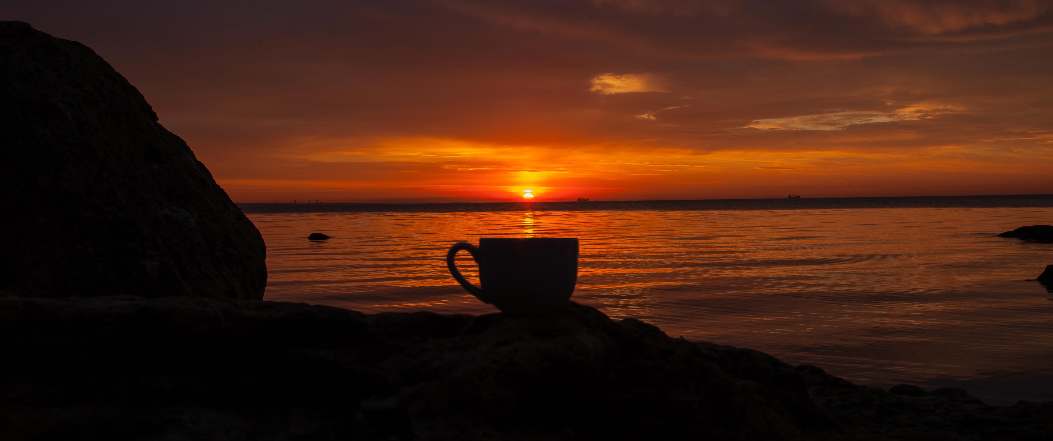 A cup of decaf coffee set against an orange sunset and California ocean.
