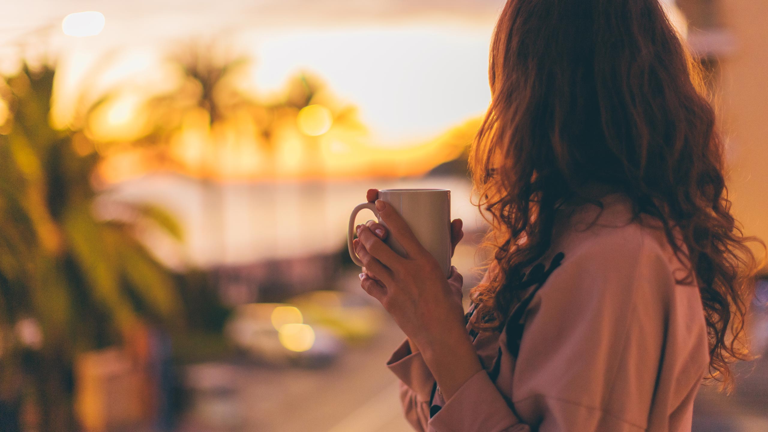 A woman drinking a cup of coffee near a California beach with palm trees